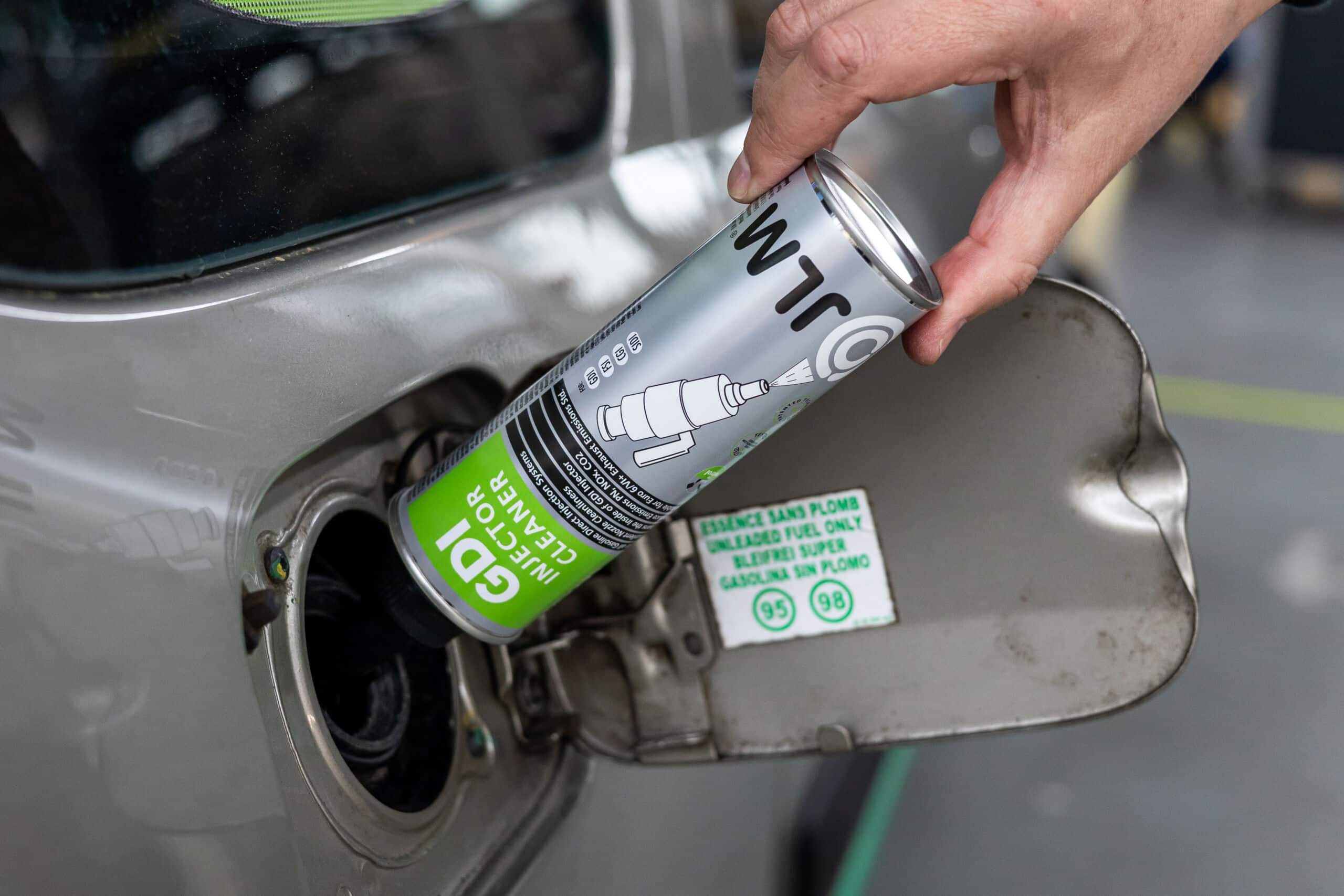 JLM GDI Injector Cleaner product bottle being inserted into the vehicle for engine care.