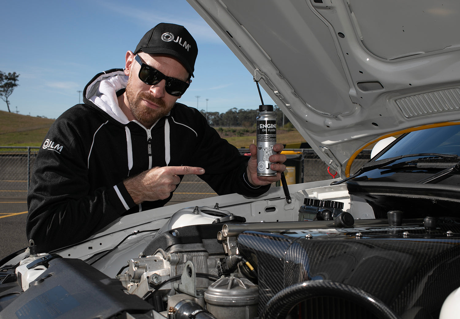 A mechanic holding a bottle of JLM Engine Oil Flush before servicing a vehicle.