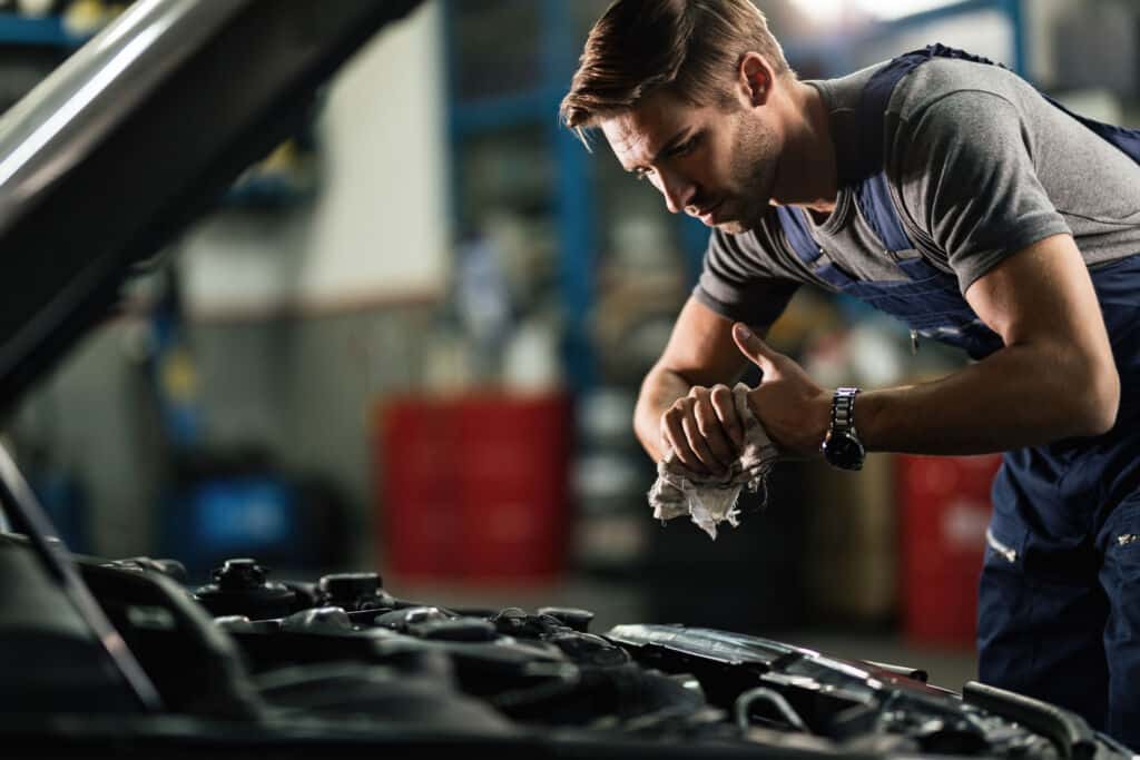 A mechanic wiping oil from his hands whilst repairing car engine in auto repair shop.